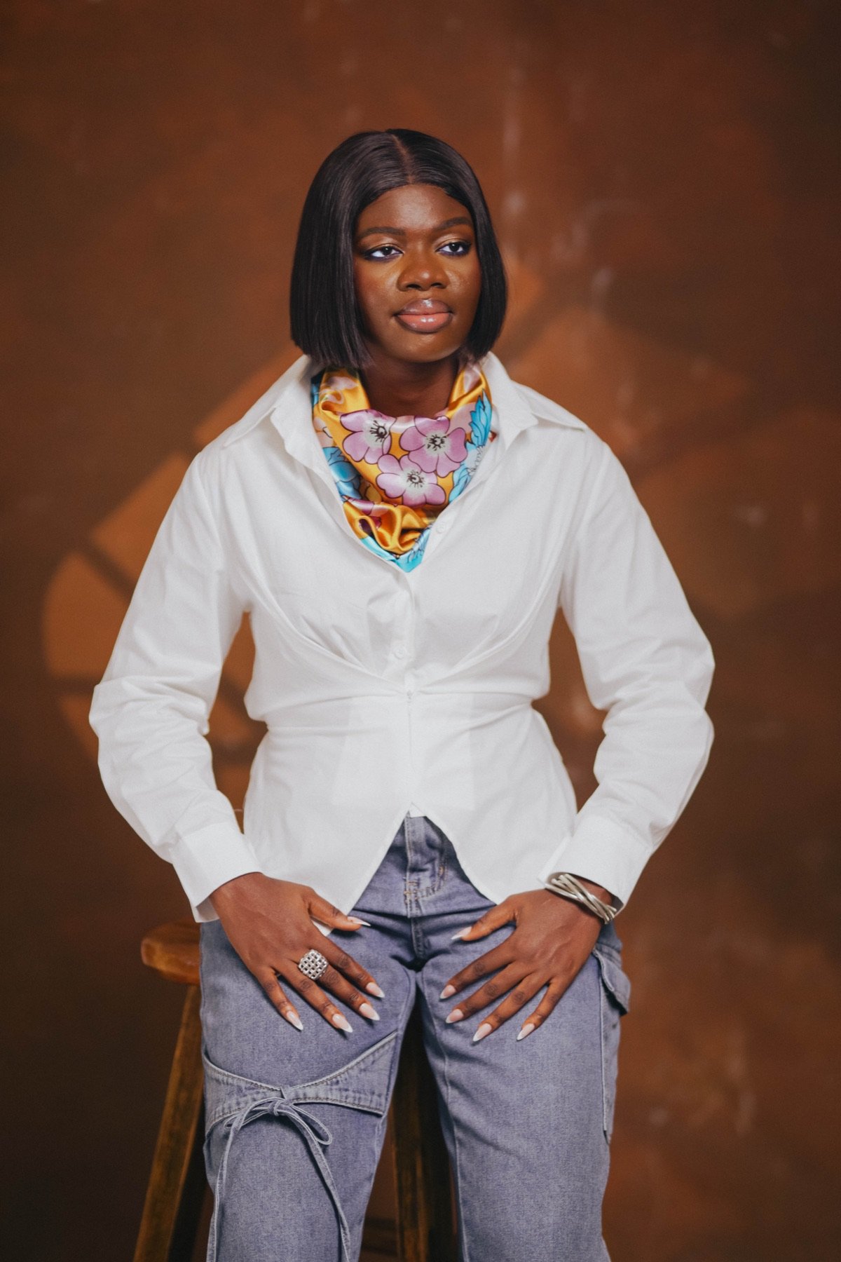 Mansa in a white shirt and silk scarf, seated on a stool