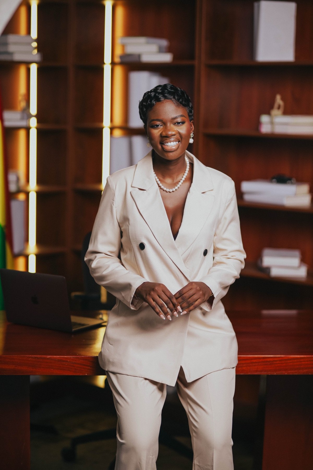 Mansa smiling at her desk in a cream suit
