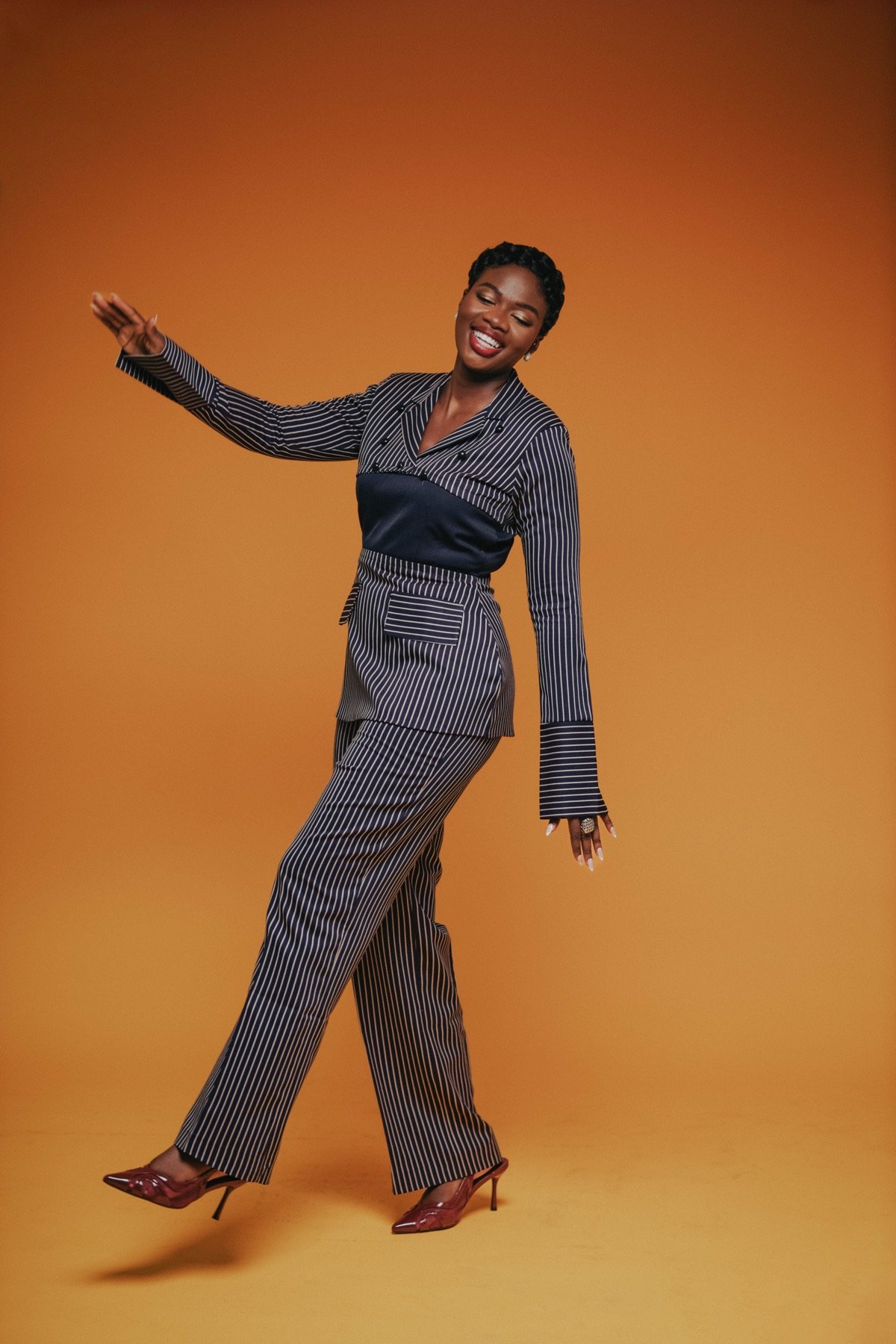 Mansa smiling mid-step against an orange backdrop