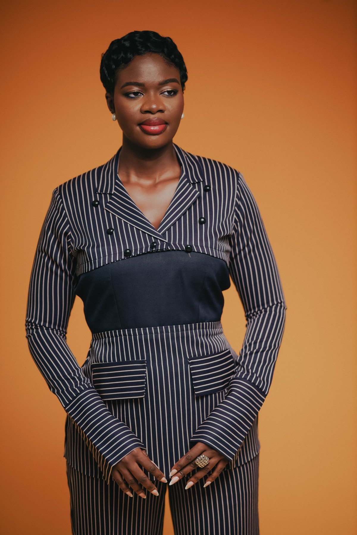 Mansa in a pinstripe suit against an orange backdrop